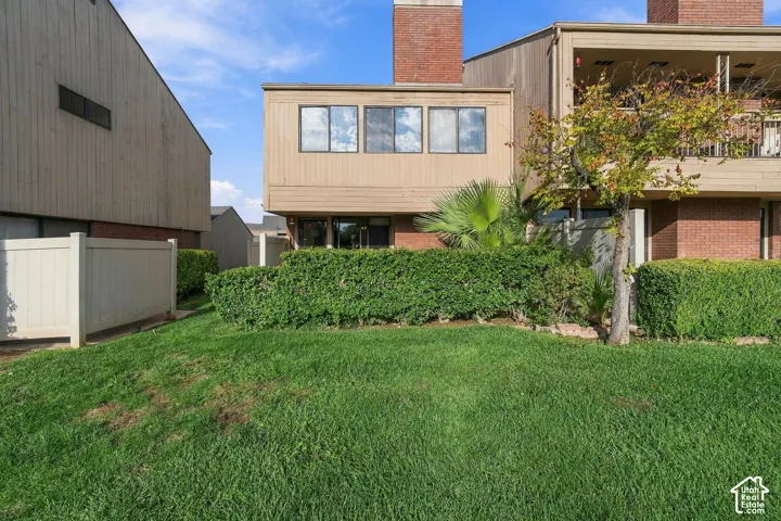 Exterior facade featuring vertical wood-finish siding, brick masonry, a brick chimney, a covered upper-level balcony, and a private rear lawn enclosed by privacy fencing