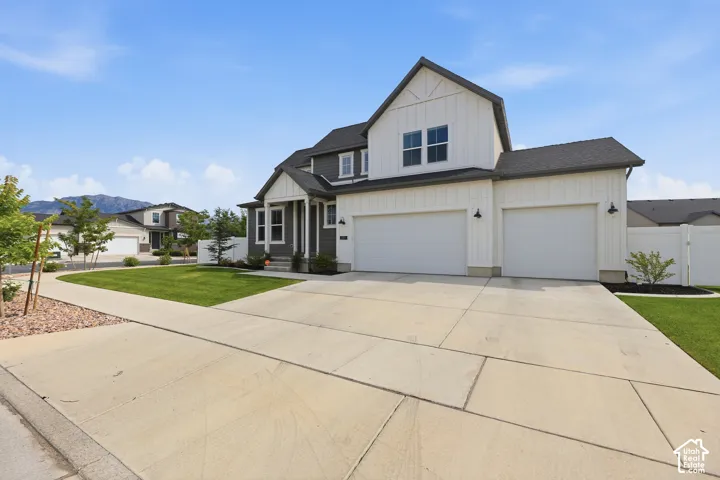 Two-story residence featuring vertical board-and-batten siding, a three-car garage, concrete driveway, and manicured landscaping