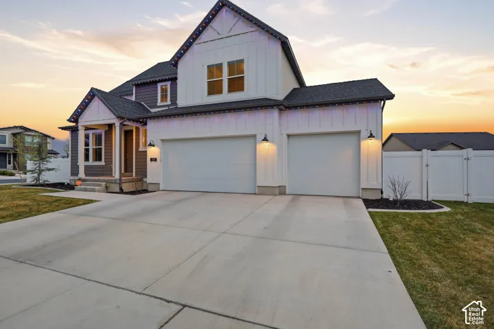 Two-story residence featuring vertical board-and-batten siding, a three-car garage, concrete driveway, and white vinyl perimeter fencing