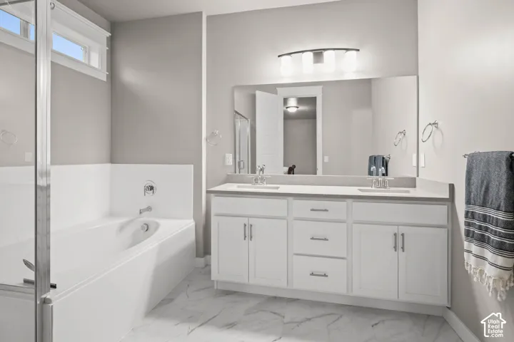 Bathroom featuring a white dual-sink vanity with a solid-surface countertop, full-width wall mirror, soaking tub, and stone-finish floor tile
