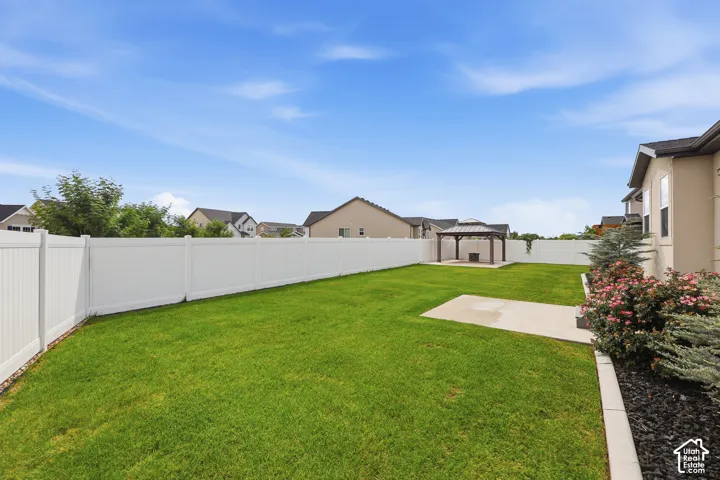 Expansive backyard featuring a white vinyl privacy fence, a concrete patio, a detached covered gazebo, and manicured landscaping