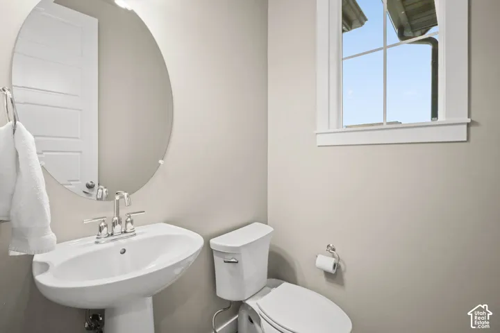 Oval frameless wall mirror, white pedestal sink, polished chrome widespread faucet, and multi-pane window with white trim