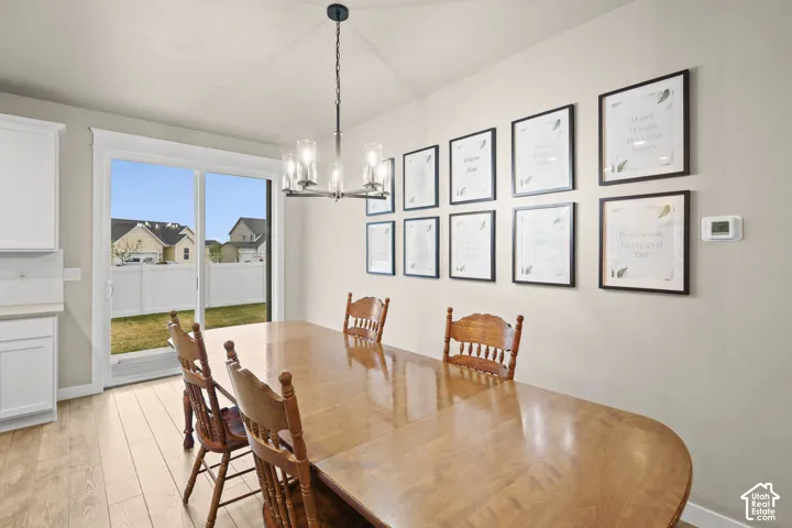 Multi-light chandelier, wood-finish flooring, and sliding glass door leading to a fenced outdoor area