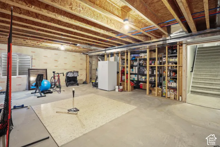 Unfinished lower level featuring exposed ceiling joists, concrete flooring, foundation wall insulation, and a carpeted staircase