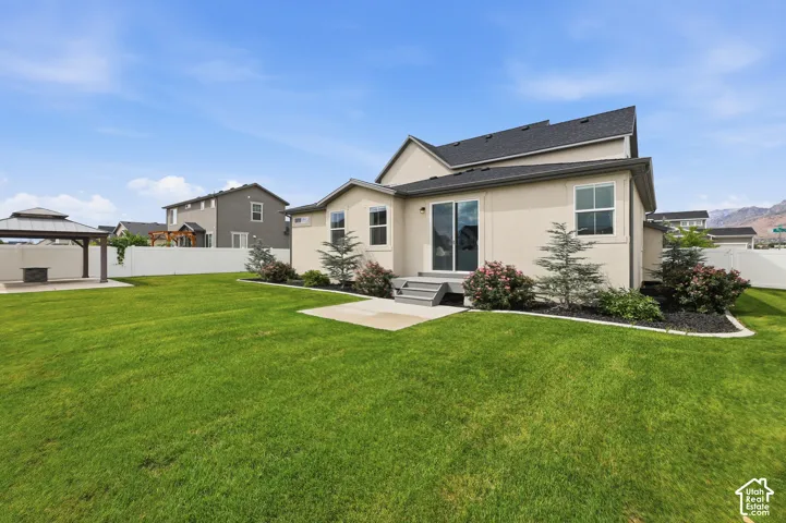 Rear exterior featuring a stucco facade, concrete patio, detached gazebo, fully fenced yard, and manicured lawn
