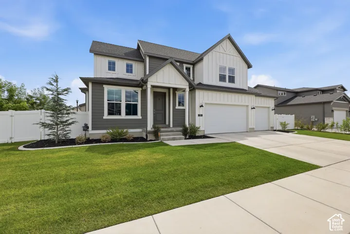 Two-story farmhouse-style exterior featuring board and batten siding, mixed-material facade, covered entryway, attached multi-car garage, and manicured front lawn