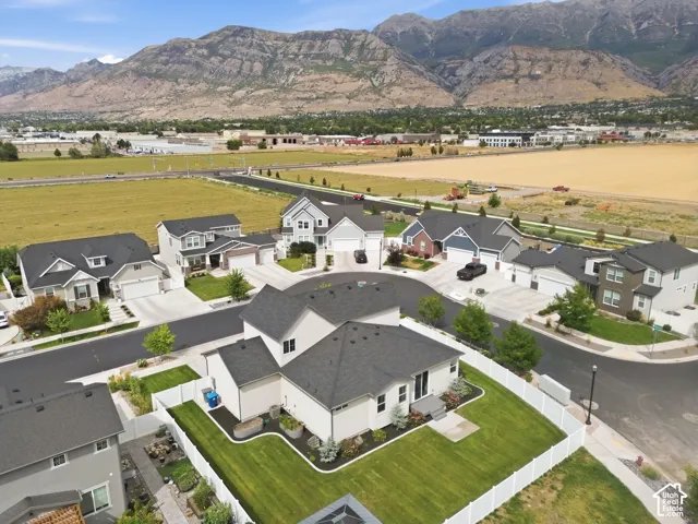 Aerial perspective of a multi-level home featuring a dark shingle roof, white vinyl perimeter fencing, and a manicured lawn