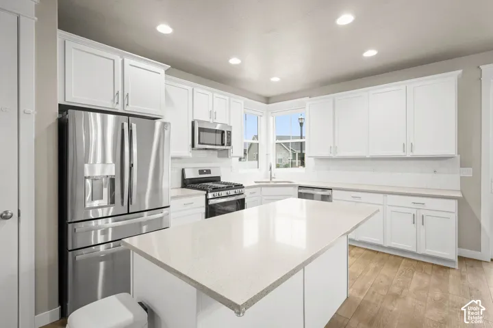 Kitchen featuring white cabinetry, an expansive central island with quartz countertops, wood-finish flooring, and stainless steel appliances including a gas range and built-in microwave