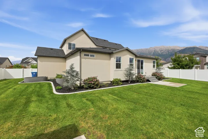Expansive backyard featuring a manicured lawn, concrete patio, perimeter vinyl fencing, metal garden beds, and mountain backdrop