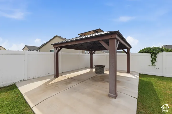 Backyard pavilion featuring a metal-roofed structure, concrete patio, and stone-finish fire pit, all enclosed by white vinyl fencing