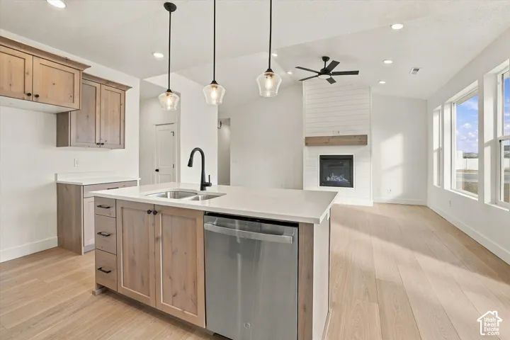 Kitchen featuring wood-finish cabinetry, an island with a light-toned countertop and stainless steel dishwasher, glass pendant lighting, wood-finish flooring, and a fireplace with a shiplap surround