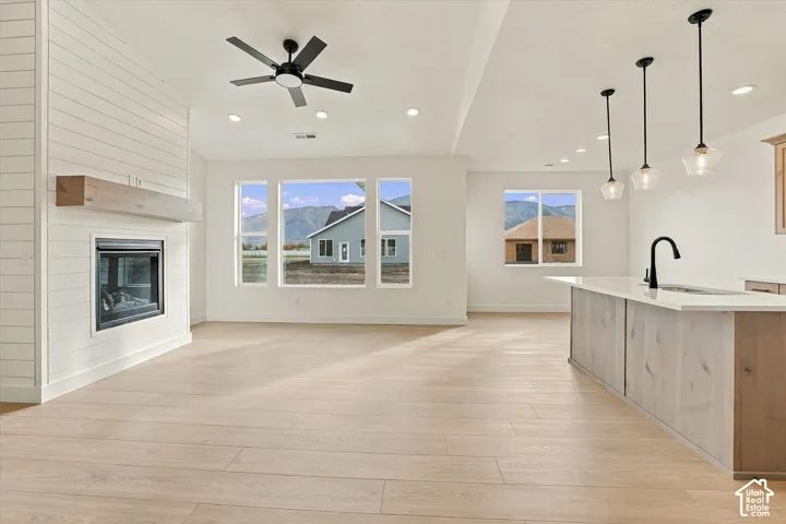 Open-concept interior featuring light-toned wood-finish flooring, a white shiplap fireplace with a wood mantel, a kitchen island with stone countertops, pendant lighting, and recessed ceiling lights