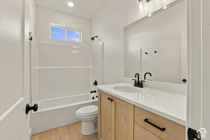 Bathroom featuring a light-tone wood-finish vanity with a stone-composite countertop, matte black fixtures, an integrated mirror, and a tub-shower combination with a surround