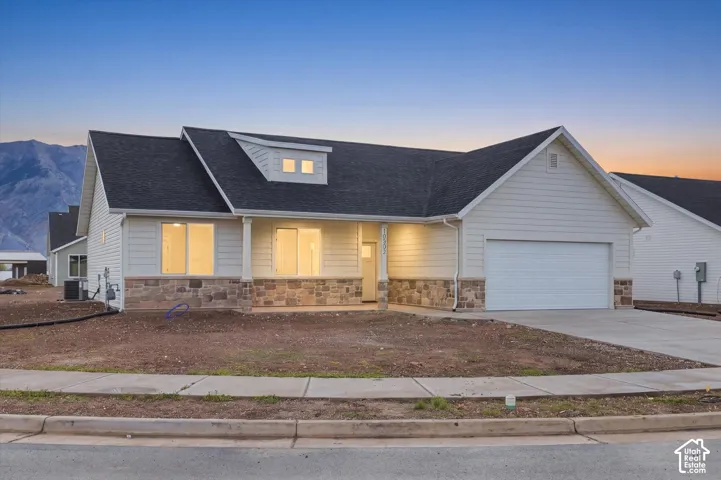 Single-level exterior featuring horizontal lap siding, stone veneer accents, a gabled roofline with a dormer, an attached garage, and mountain backdrop