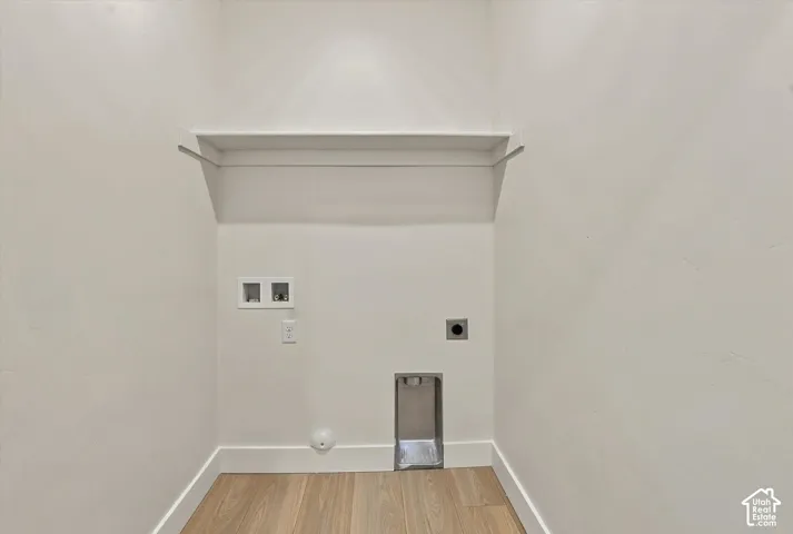 Dedicated utility area featuring wood-finish flooring, a wall-mounted shelf, and integrated plumbing and electrical hookups