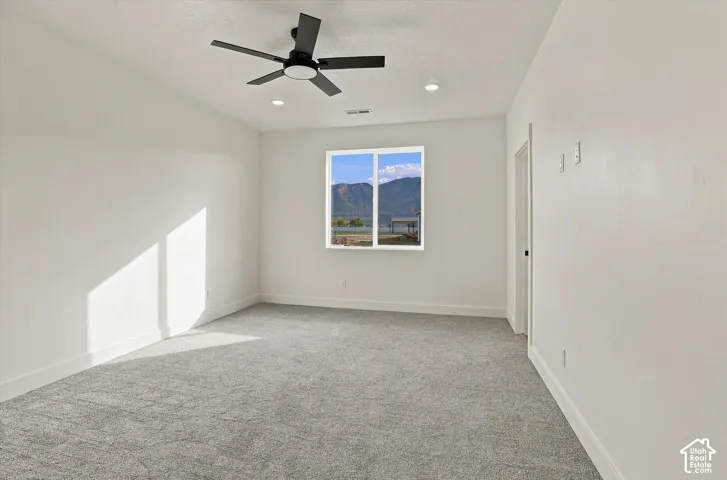 Neutral-toned carpeted flooring, multi-blade ceiling fan with integrated lighting, recessed lighting, and mountain scenery visible through a single-pane window