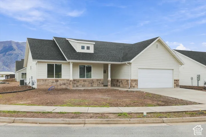 Single-story residence featuring a combination of horizontal siding and stone masonry, a shingled roof with a dormer window, an attached two-car garage, and a concrete driveway