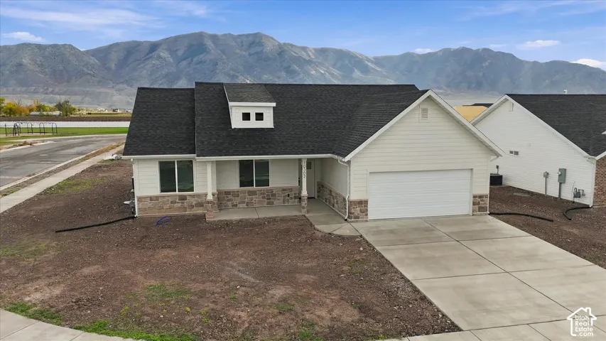 Single-story residence featuring horizontal siding, stone veneer accents, an asphalt shingle roof, a two-car garage, and mountain range scenery