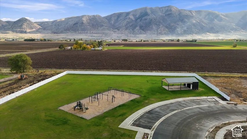 Expansive fenced recreational area featuring a playground, an open-air pavilion, manicured lawn, and mountain scenery
