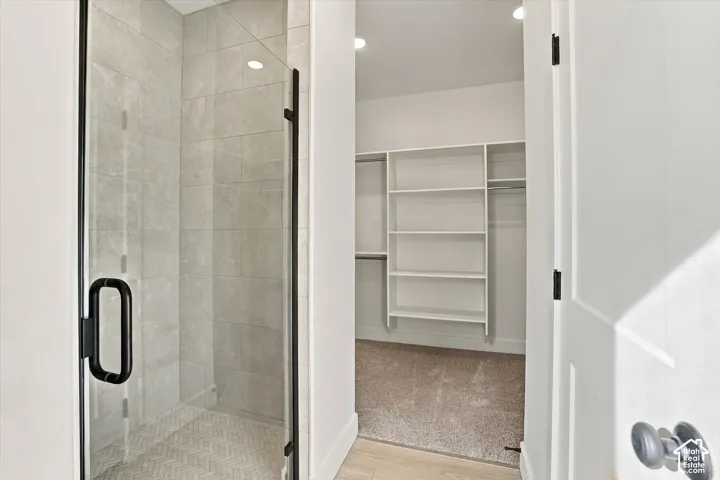 Walk-in shower featuring floor-to-ceiling tile, herringbone-patterned shower floor, and a matte black framed glass door, paired with a built-in walk-in closet shelving system