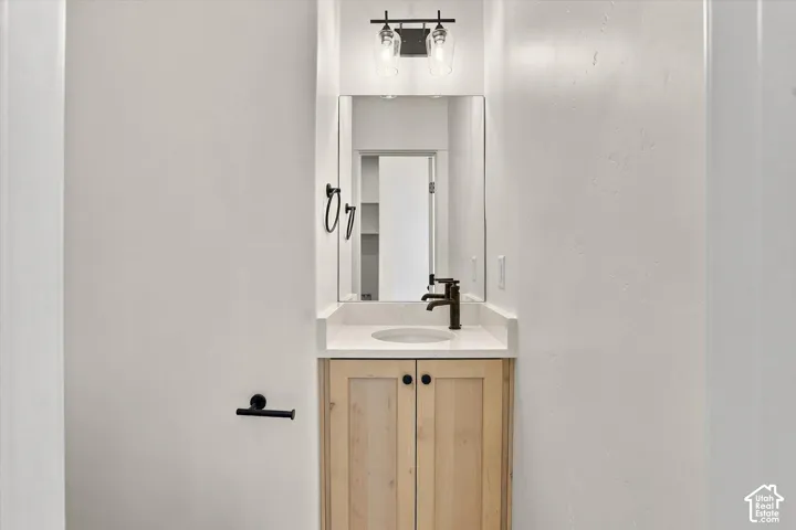 Vanity featuring light wood-finish cabinetry, a rectangular quartz countertop, integrated basin, matte black faucet, and a wall-mounted light fixture with glass shades