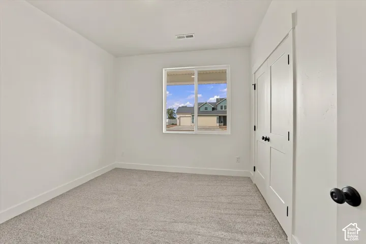 Neutral interior space featuring wall-to-wall carpeting, dual-panel closet doors with matte black hardware, and a sliding window