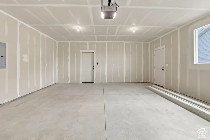 Attached garage with concrete flooring, finished drywall, overhead garage door opener, and natural lighting provided by a side window