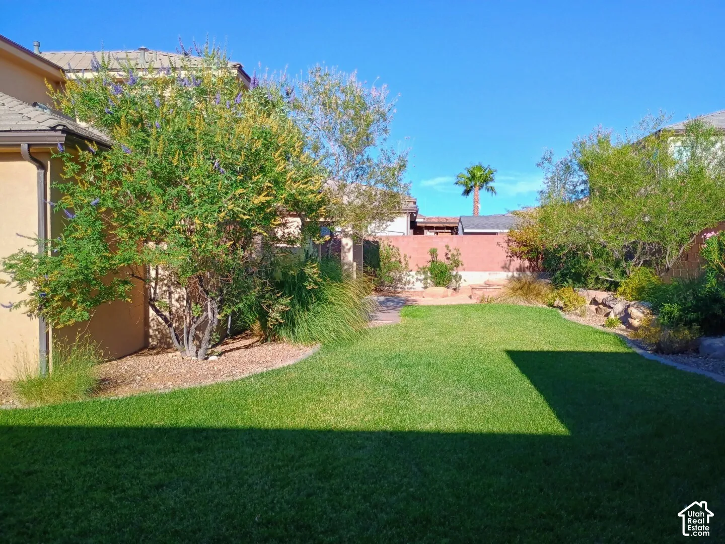 Backyard featuring a manicured lawn, mature landscaping, gravel garden beds, and a masonry perimeter wall