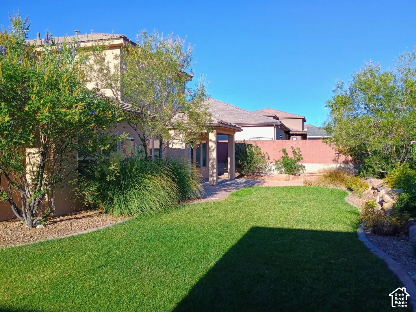 Landscaped backyard featuring a stone-paver patio, mature trees, ornamental grasses, and perimeter wall