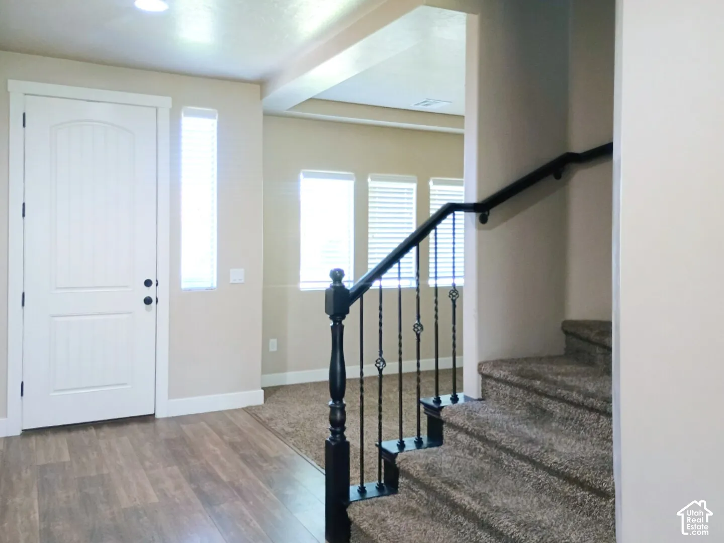 Foyer featuring wood-finish flooring, a white panel entry door, carpeted staircase with a decorative metal balustrade, and recessed lighting