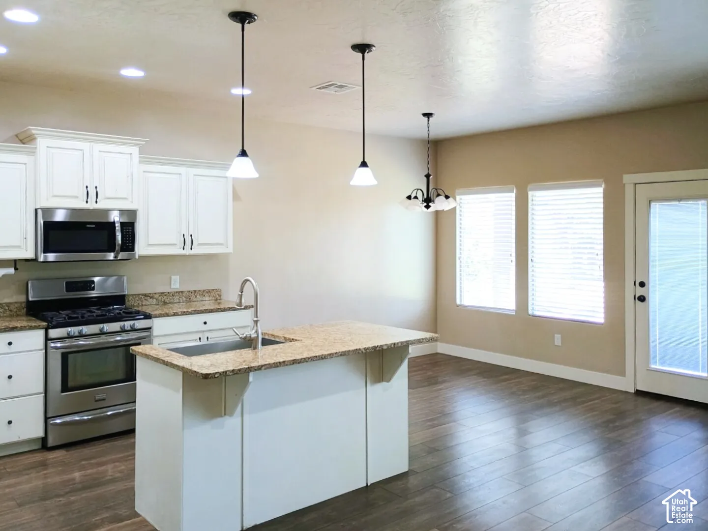 Kitchen featuring white cabinetry, stone countertops, stainless steel appliances, a center island with an integrated sink, and wood-finish flooring