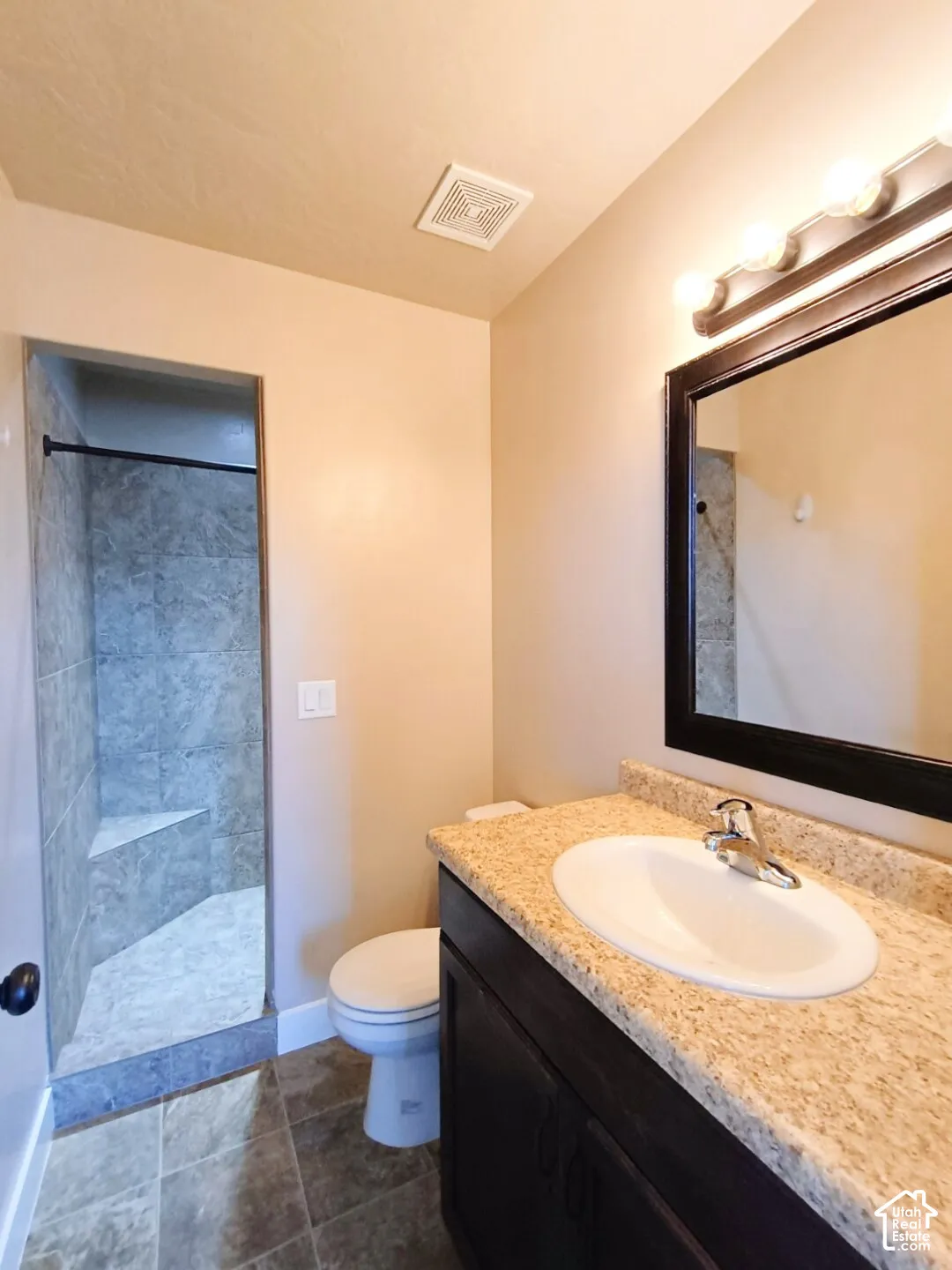 Bathroom featuring a dark-finish vanity with a stone-composite countertop, oval drop-in sink, framed mirror, and tiled shower enclosure with integrated bench seating