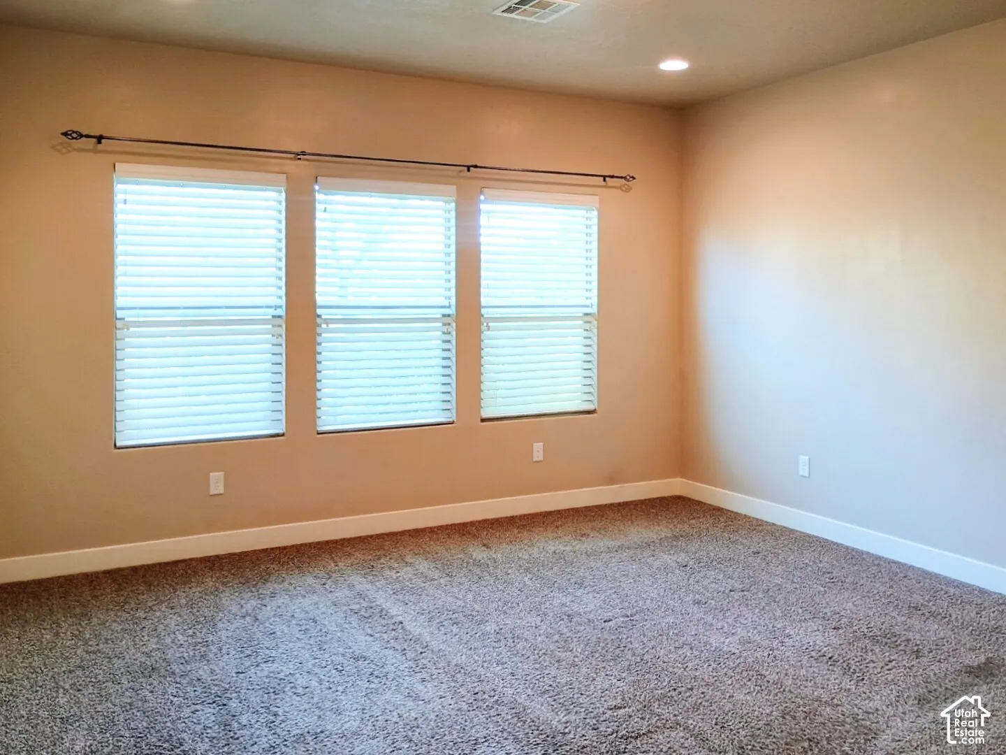 Room interior featuring neutral wall paint, wall-to-wall carpeting, three multi-pane windows with horizontal blinds, and recessed lighting