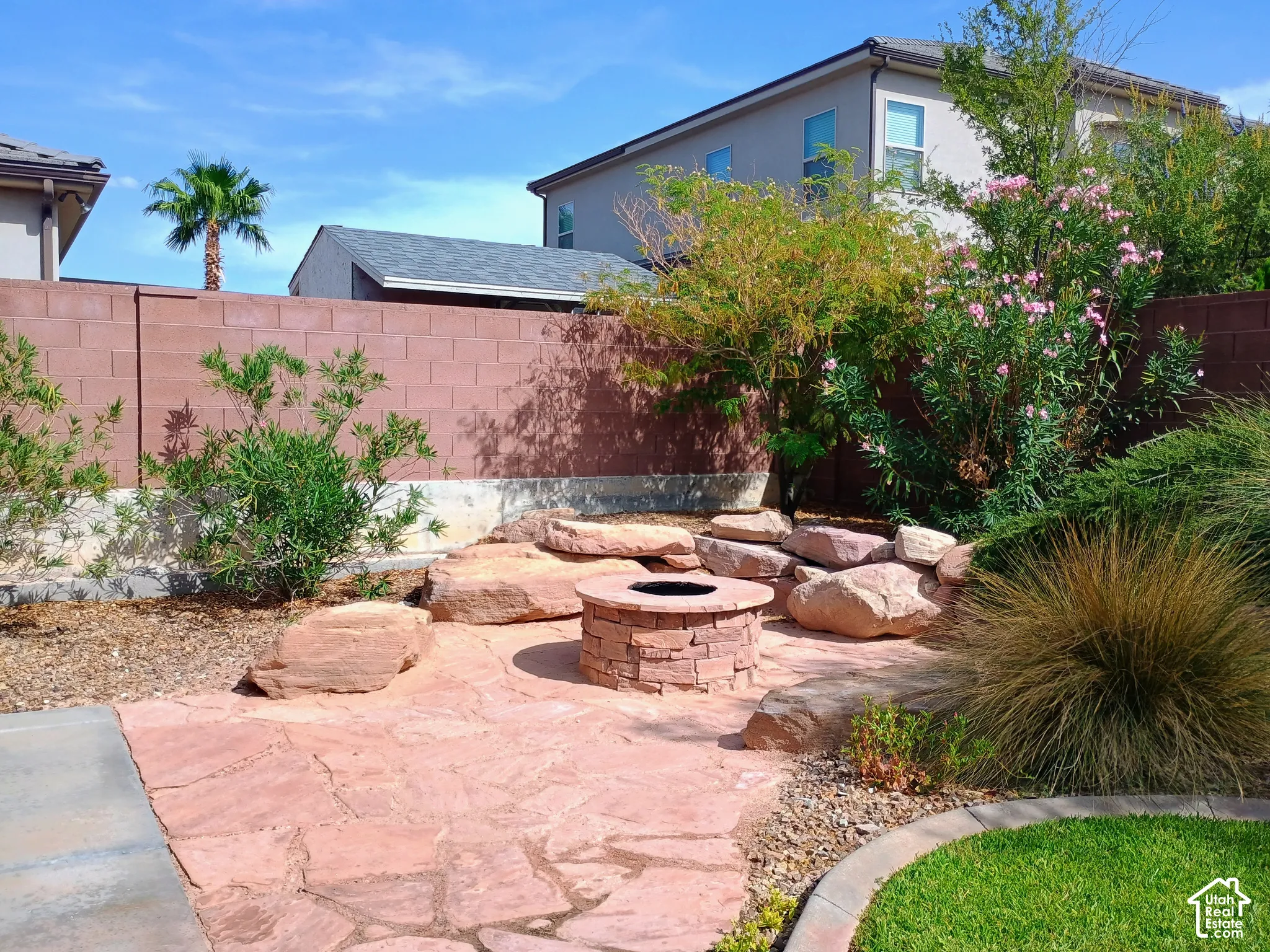 Flagstone patio featuring a built-in stone fire pit, tiered landscaping with large natural boulders, and a masonry perimeter wall