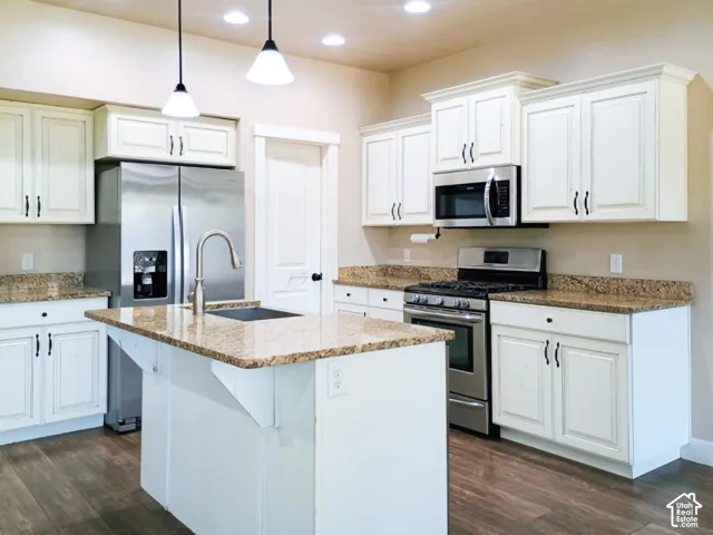 Kitchen featuring a center island, stone-finish countertops, stainless steel appliances, white cabinetry with crown molding, and wood-finish flooring
