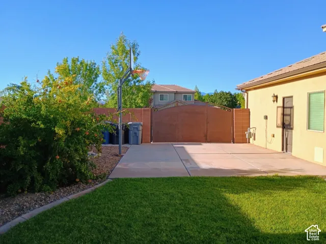 Exterior side yard featuring a concrete pad, gated access, masonry perimeter wall, and mature landscaping