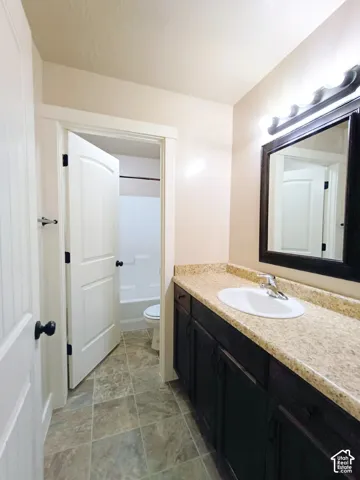 Bathroom featuring a dark-toned vanity, stone-finish countertop with an integrated oval sink, multi-light wall-mounted fixture, and tile flooring