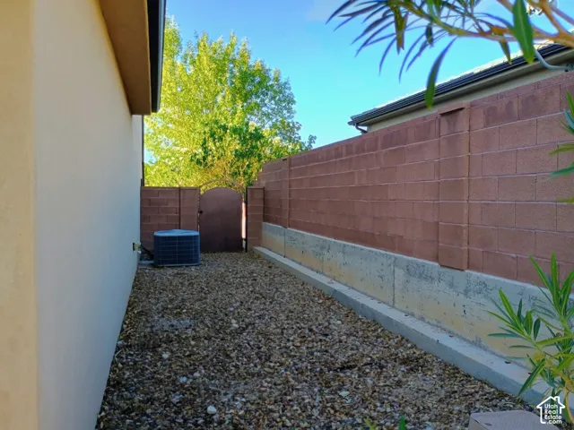 Side yard featuring a gravel surface, concrete retaining wall, decorative masonry block perimeter fence, and metal pedestrian gate