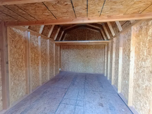 Outbuilding interior featuring exposed structural framing, oriented strand board wall panels, a gambrel roofline, and an elevated storage loft