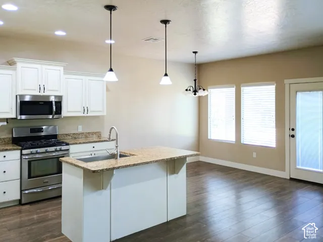 Kitchen featuring white cabinetry, stone countertops, stainless steel appliances, a center island with an integrated sink, and wood-finish flooring