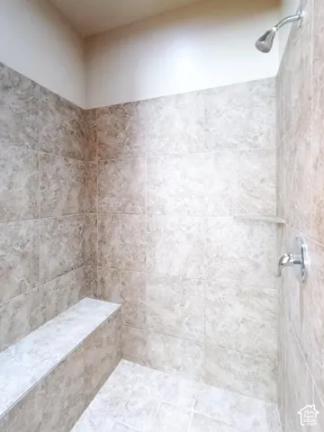 Walk-in shower featuring floor-to-ceiling tile surrounds, integrated tiled bench seating, built-in shelving, and a chrome wall-mounted fixture