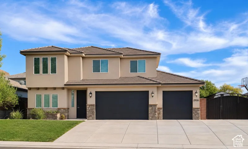 Two-story exterior featuring a stucco facade, stone veneer accents, multi-car garage, concrete driveway, and tile roof