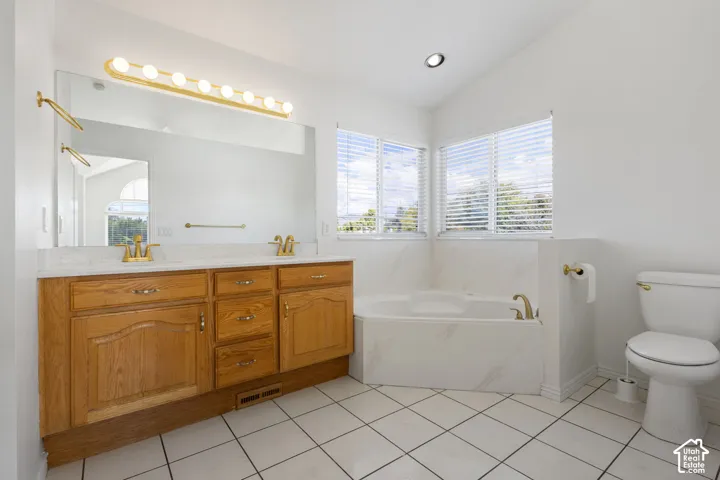 Dual-sink vanity with wood-finish cabinetry, countertop with integrated basins, jetted corner tub with stone-finish surround, ceramic tile flooring, and metallic finish fixtures