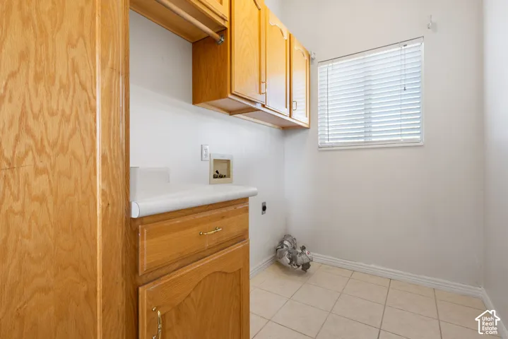 Laundry area featuring natural wood cabinetry, solid surface countertop, tile flooring, and window with attached blinds