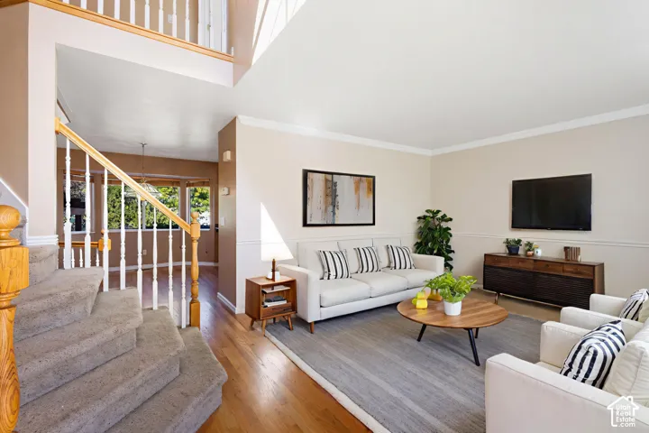 High-ceiling living area featuring wood-finish flooring, chair rail molding, and a staircase with white balusters and a wood-finish handrail