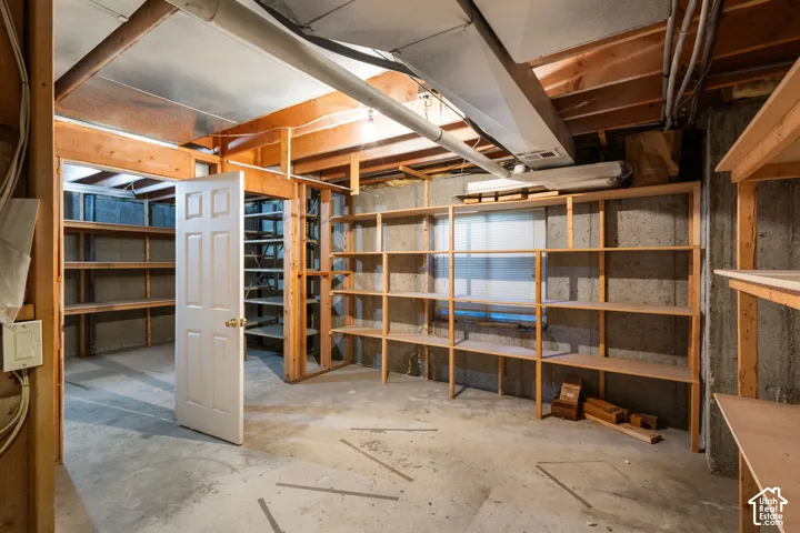 Unfinished utility room featuring concrete flooring, concrete masonry unit walls, integrated wood-frame shelving units, and a six-panel interior door