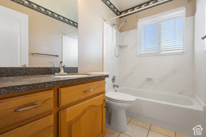 Bathroom featuring a vanity with dark stone-finish countertop, an integrated sink, a full-width mirror, tile flooring, and a tub-shower combination with surround wall paneling