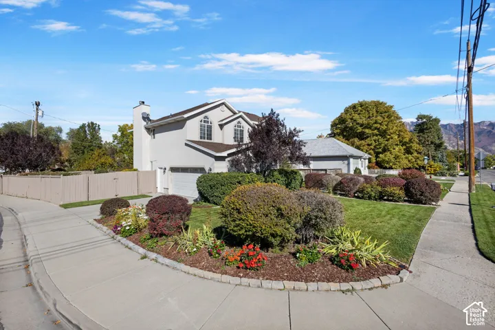 Two-story exterior featuring a light-toned stucco facade, arched windows, an attached two-car garage, and landscaped grounds with mature shrubbery
