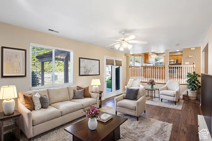 Open-concept living space featuring wood-finish flooring, white ceiling fan with integrated lighting, dual-pane windows, and a classic white spindle railing partition