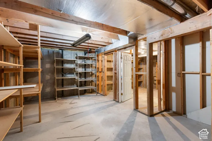 Unfinished lower-level space featuring concrete foundation walls, exposed wood framing, concrete flooring, and overhead task lighting